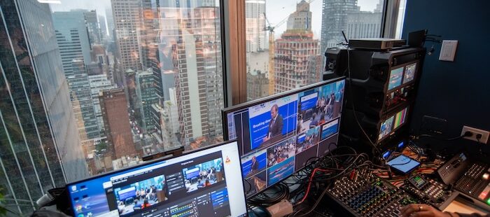 The view through a window in a skyscraper in the NewYork looking across the skyline. In the foreground there is a livestream audio and video mixing desk.