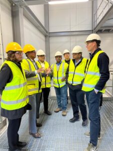 a group of people in yellow high viz vests and hard hats are talking in a factory.